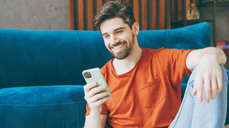 Homem sentado, sorrindo, mexendo no celular e acessando o aplicativo Hapvida NotreDame Intermédica Minas