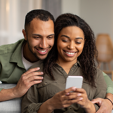 Homem e mulher acessam o celular juntos e sorriem