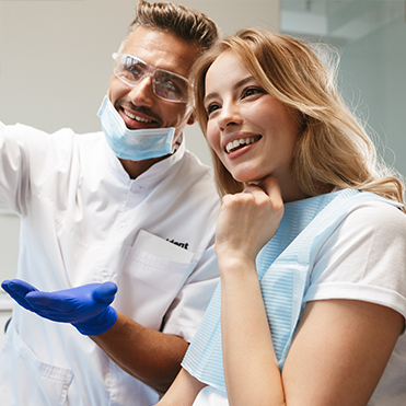 Dentista e paciente sorriem em consultório odontológico