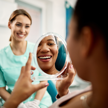 Mulher olha sorriso pelo espelho em consultório odontológico