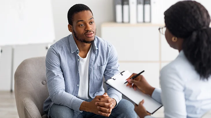 Homem negro sentado conversando com psiquiatra mulher em sessão de atendimento