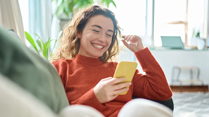 Mulher jovem sorrindo ao olhar conteúdo no celular e ver os benefícios de contratar planos de sáude e odontológico juntos