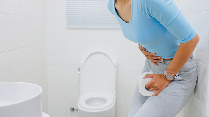 Pessoa com a mão na barriga, cruzando a perna e segurando o papel higiênico