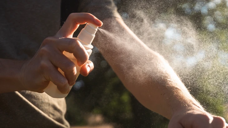 Pessoa espirrando repelente no braço