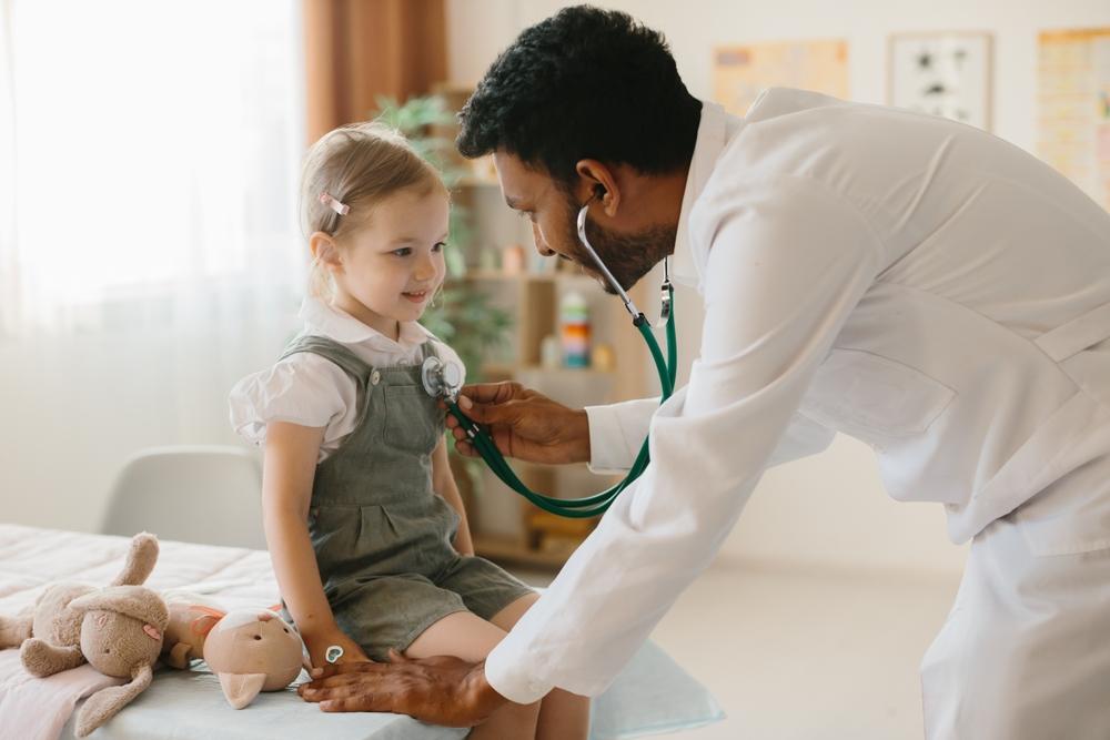 Criança em consulta com profissional de saúde usando estetoscópio, destacando atendimento pneumológico e tratamento de doenças respiratórias crônicas.