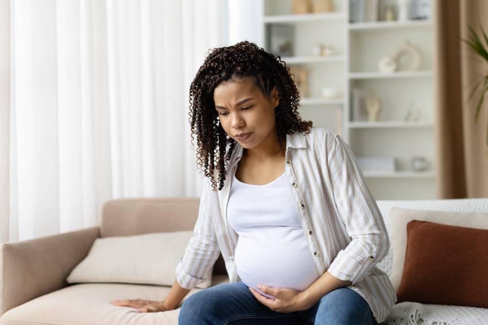 Mulher grávida sentada no sofá, com a mão no abdômen, atenta a possíveis sinais de sangramento vaginal durante a gestação.