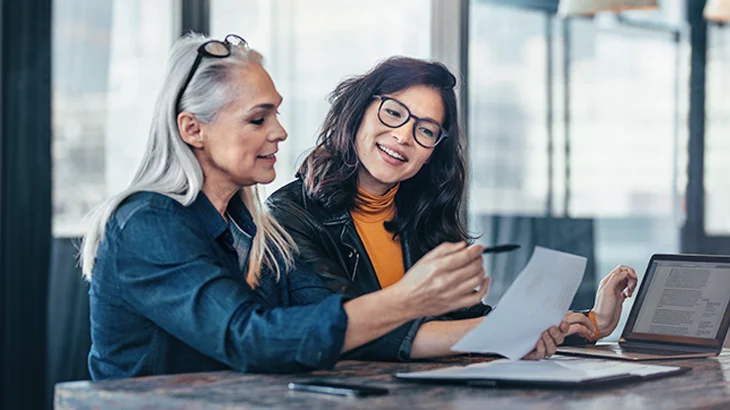 Duas mulheres de negócio sorrindo, sentadas e analisando documento
