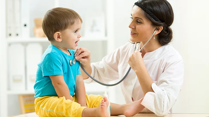Doutora examinando menino com estetoscópio na região torácica