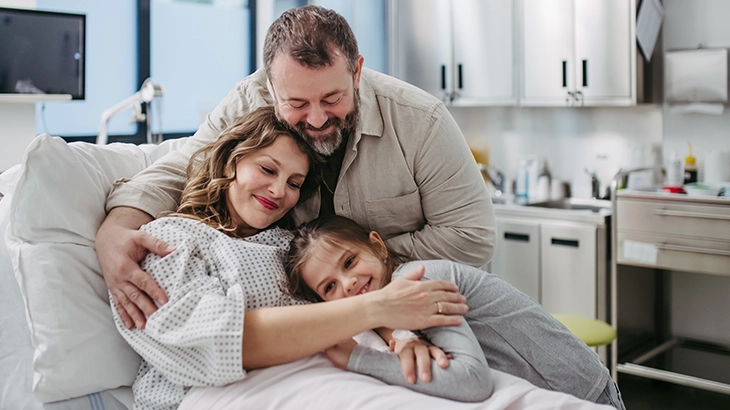 Familia se abraçando feliz no leito de um hospital.